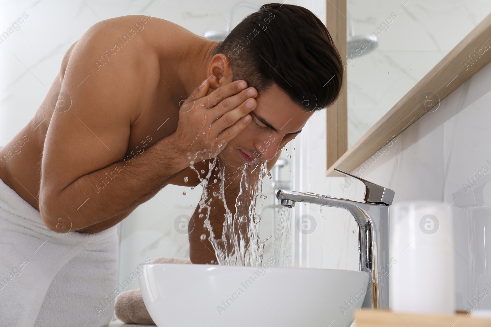 Photo of Handsome man washing face over sink in bathroom