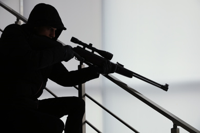 Photo of Hired professional killer with sniper rifle indoors