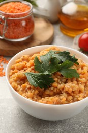 Photo of Delicious red lentils with parsley in bowl on light grey table, closeup