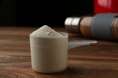 Measuring scoop of protein powder on wooden table, closeup