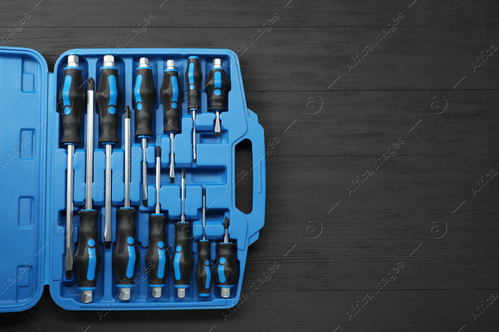 Photo of Set of screwdrivers in open toolbox on black wooden table, top view. Space for text