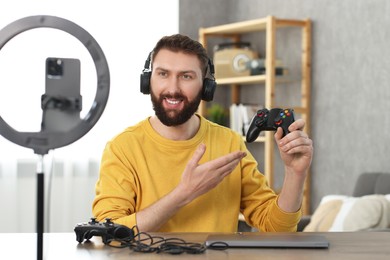 Photo of Smiling technology blogger recording video review about game controllers at home