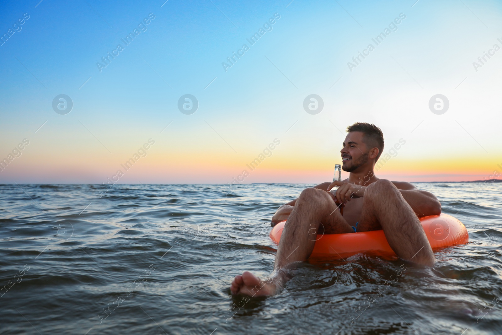 Photo of Happy young man with drink on inflatable ring in water