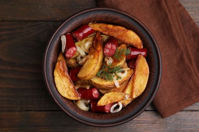 Photo of Delicious baked potato with thin dry smoked sausages, onion and dill in bowl on wooden table, top view