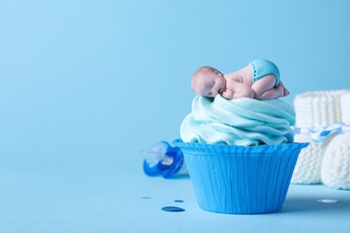 Photo of Beautifully decorated baby shower cupcake with cream and boy topper on light blue background. Space for text