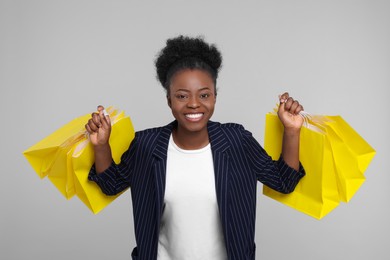 Happy young woman with shopping bags on light grey background