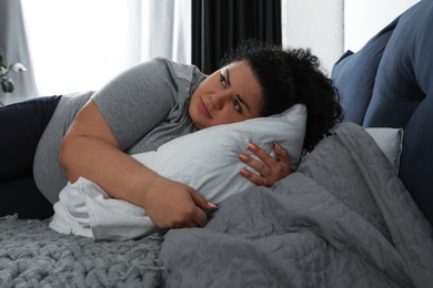 Photo of Depressed overweight woman hugging pillow on bed
