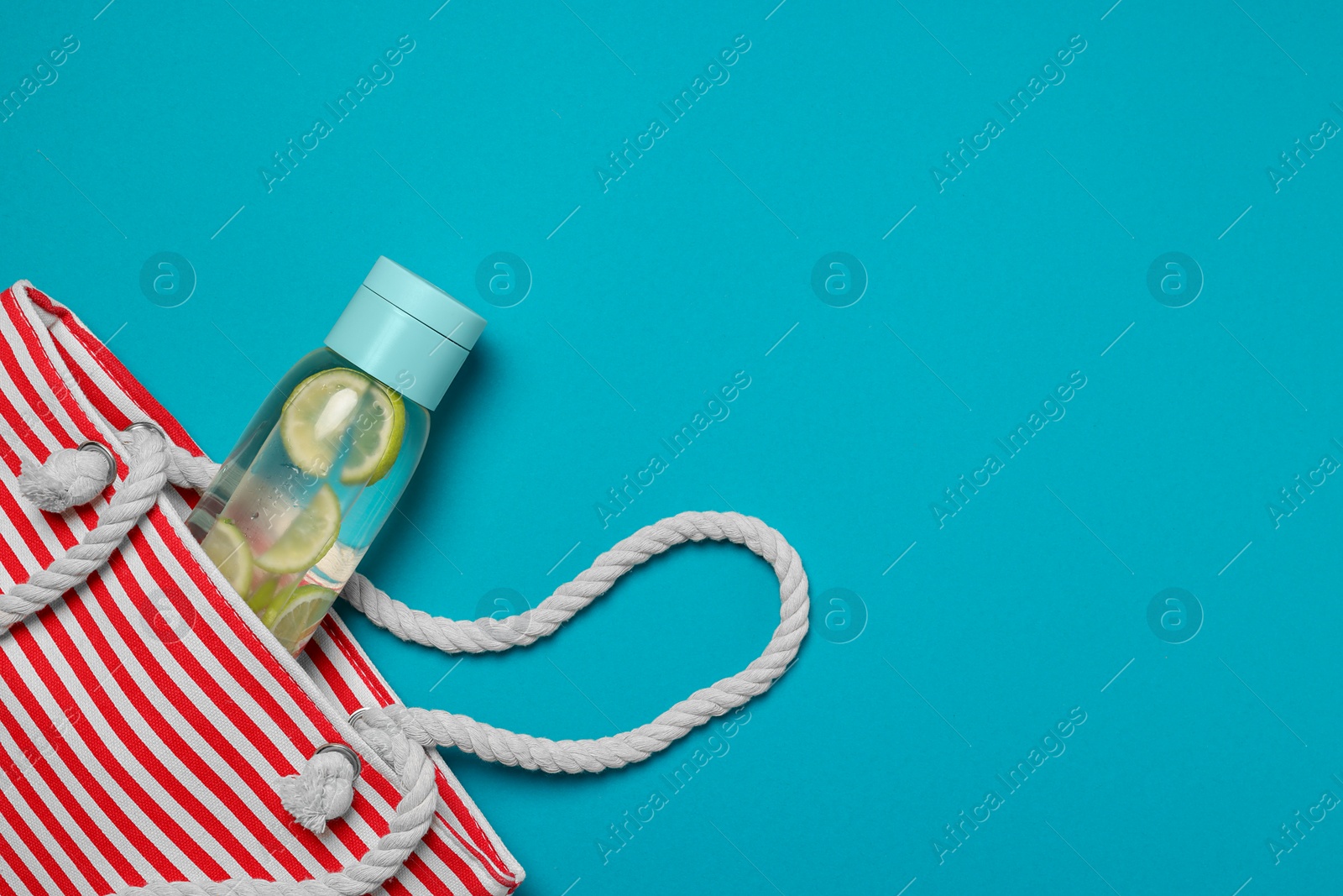 Photo of Beach bag and bottle with refreshing drink on light blue background, flat lay. Space for text