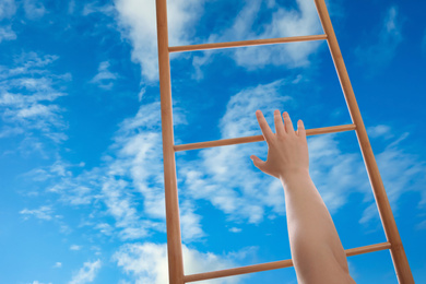 Image of Woman climbing up wooden ladder against blue sky with clouds, closeup