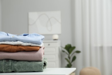 Photo of Stack of different folded clothes on table indoors, closeup. Space for text
