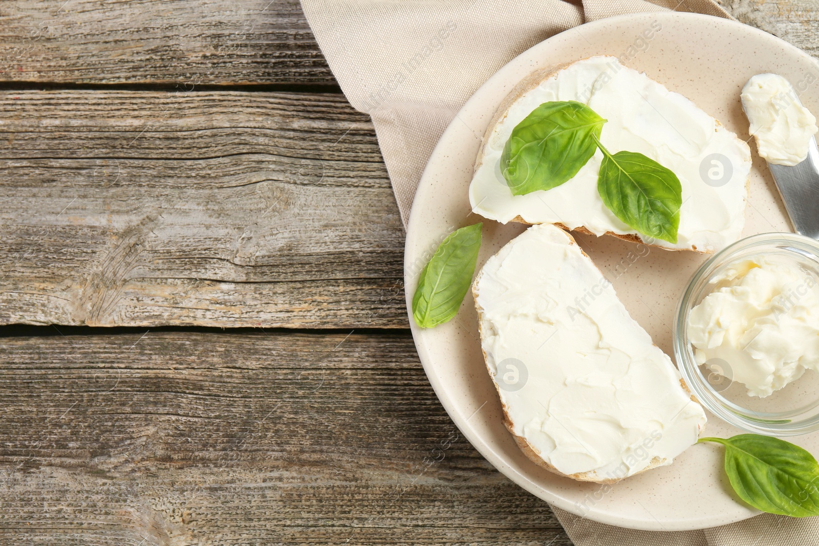 Photo of Delicious sandwiches with cream cheese and basil leaves on wooden table, top view. Space for text