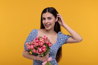 Happy young woman with beautiful bouquet on orange background