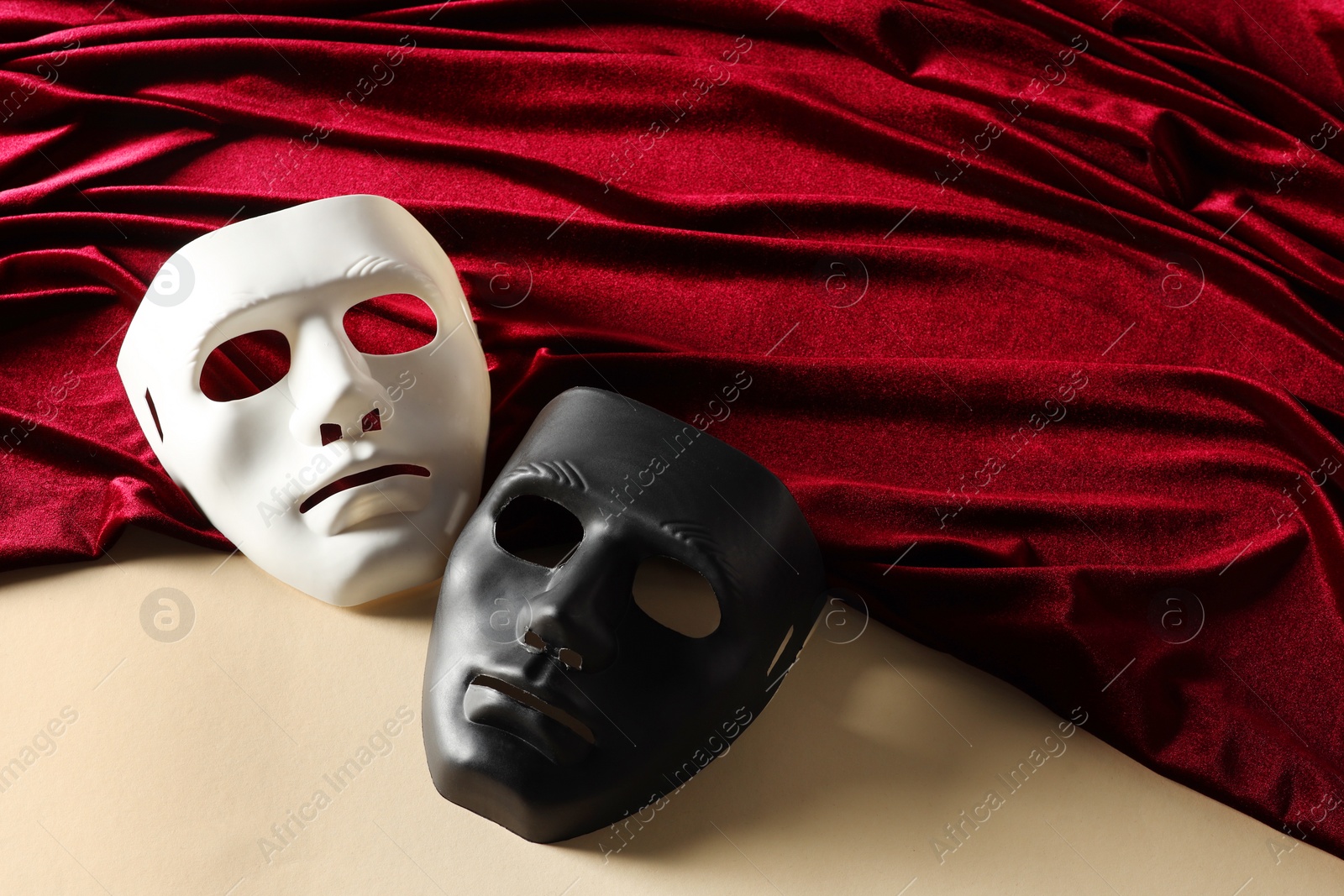 Photo of Theater arts. Two masks and red fabric on beige background, above view