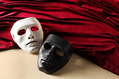 Photo of Theater arts. Two masks and red fabric on beige background, above view