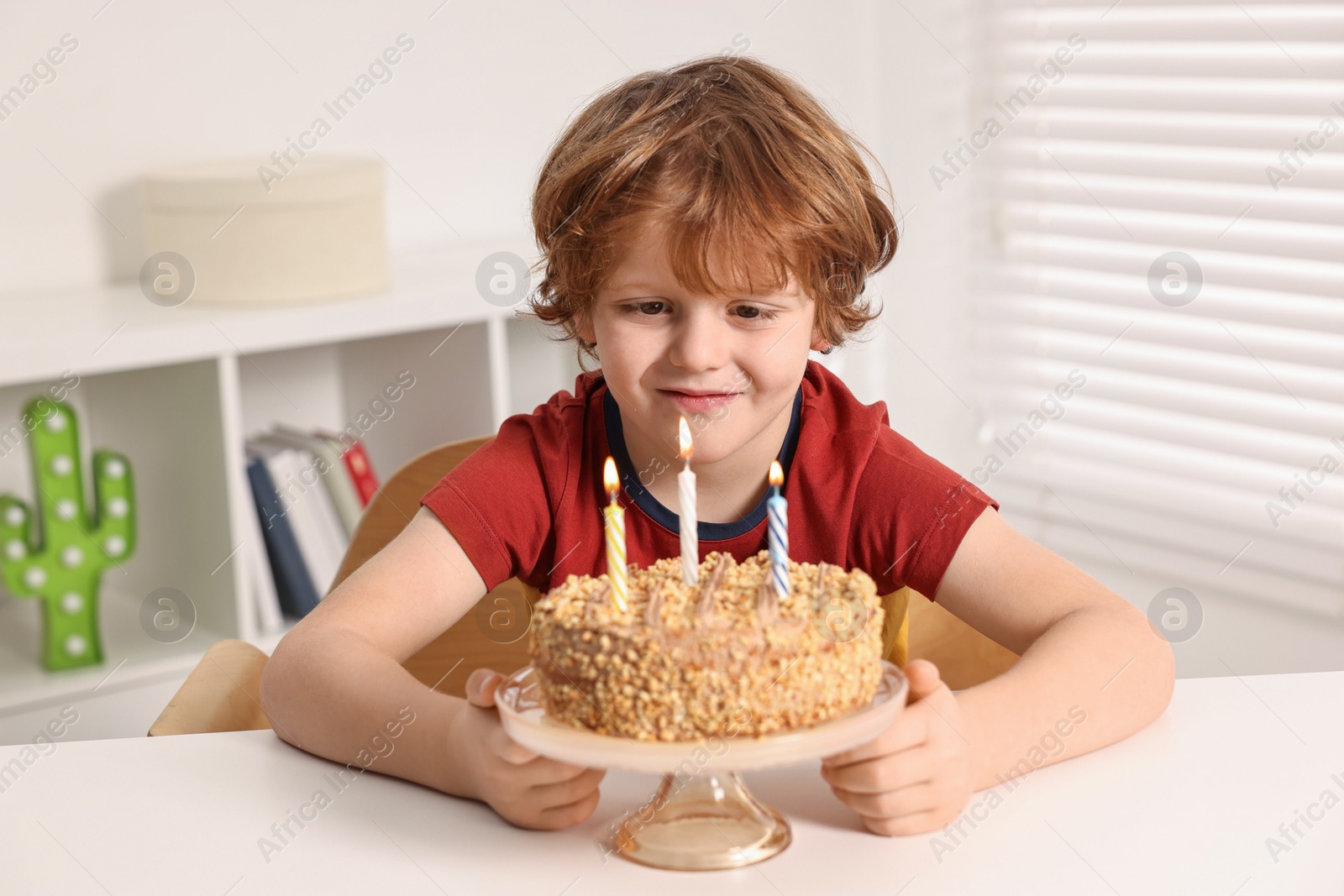 Photo of Cute boy with birthday cake at table indoors