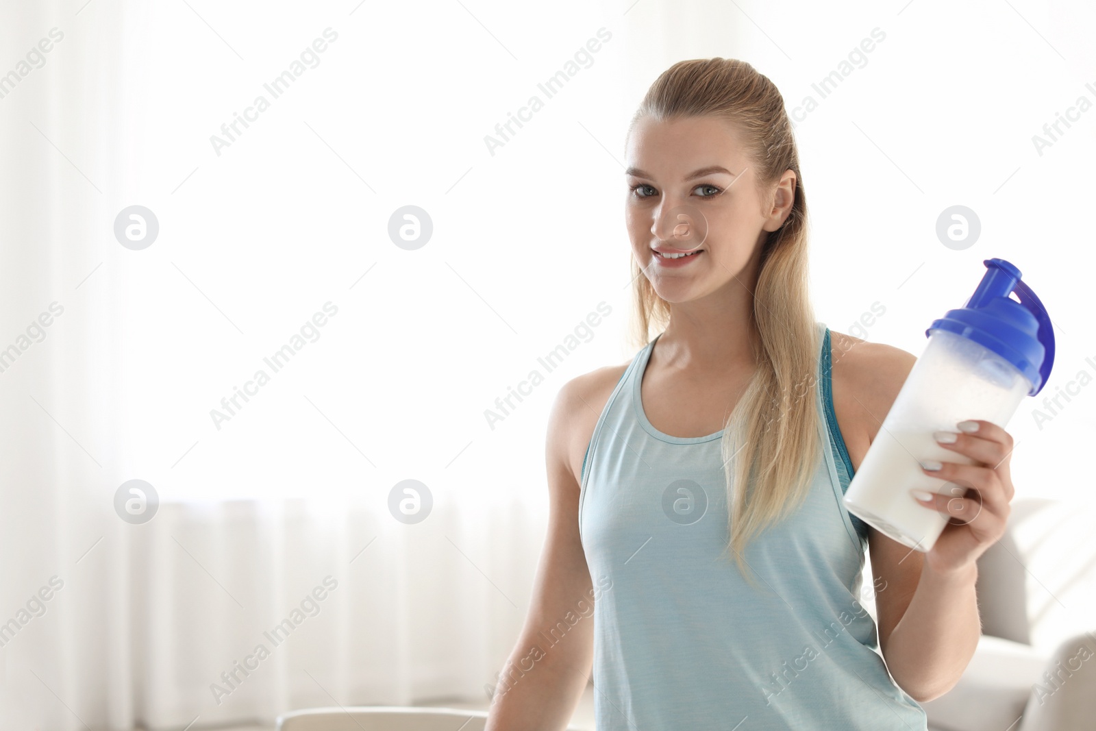 Photo of Young woman holding bottle of protein shake in light room. Space for text