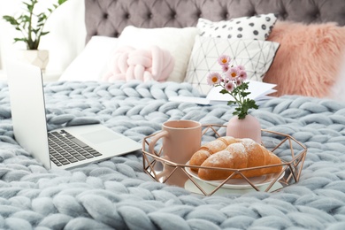 Tray with tasty breakfast and laptop on bed