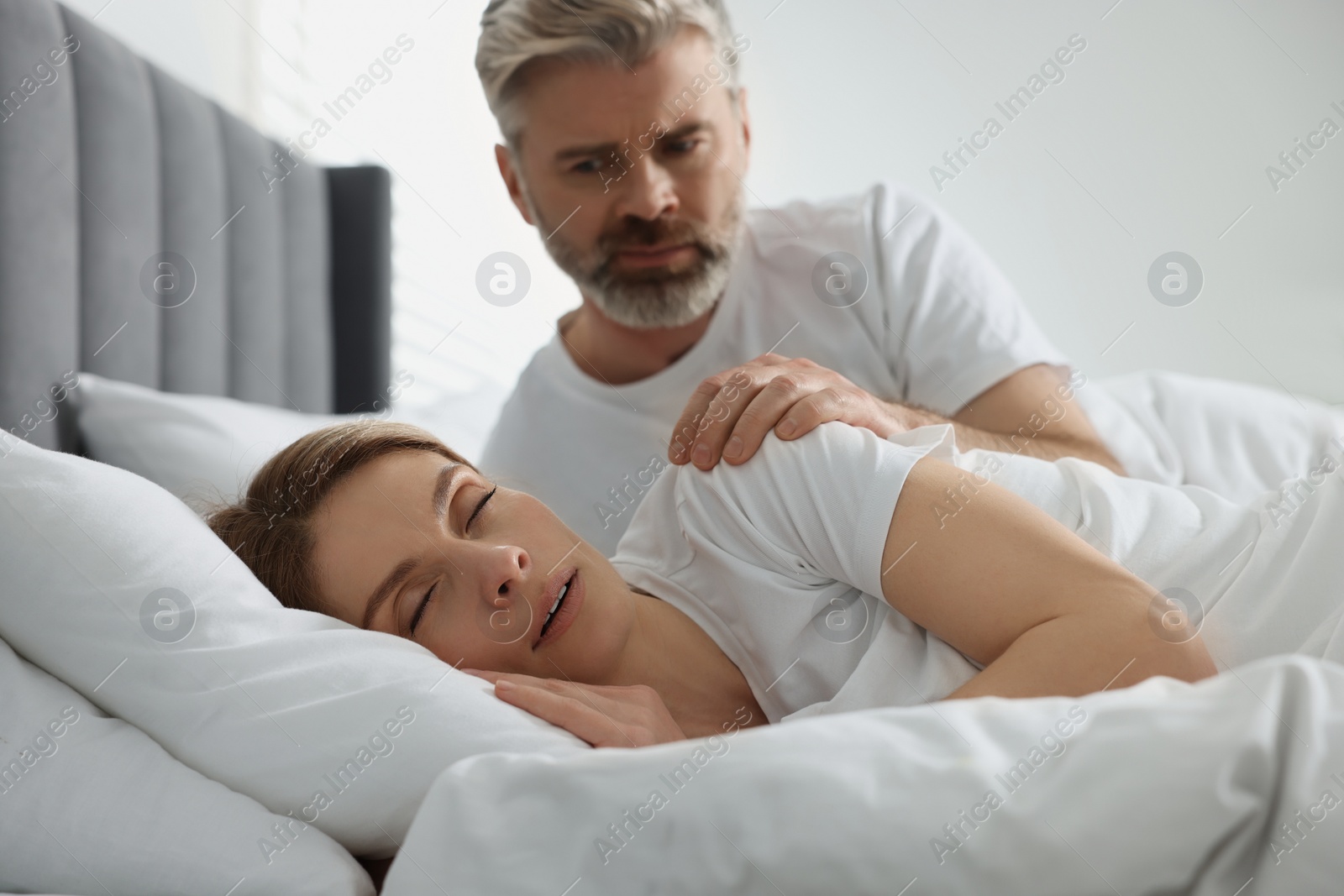 Photo of Irritated man waking up his snoring wife in bed at home