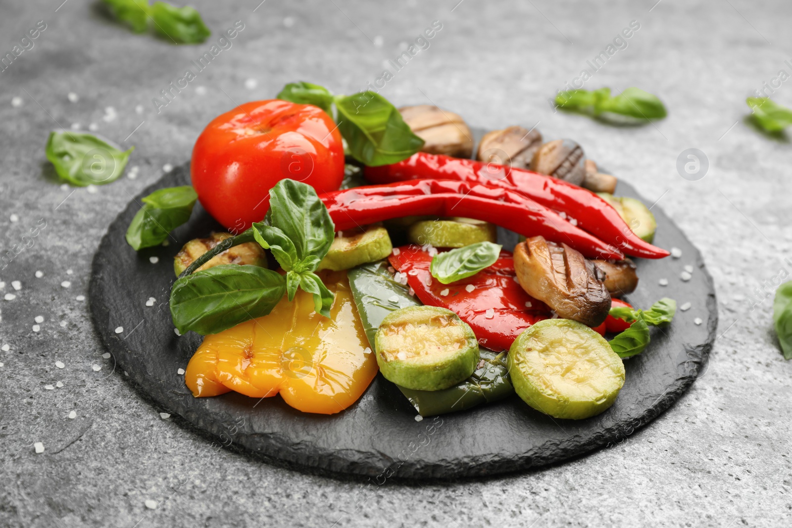 Photo of Delicious grilled vegetables with basil on grey table