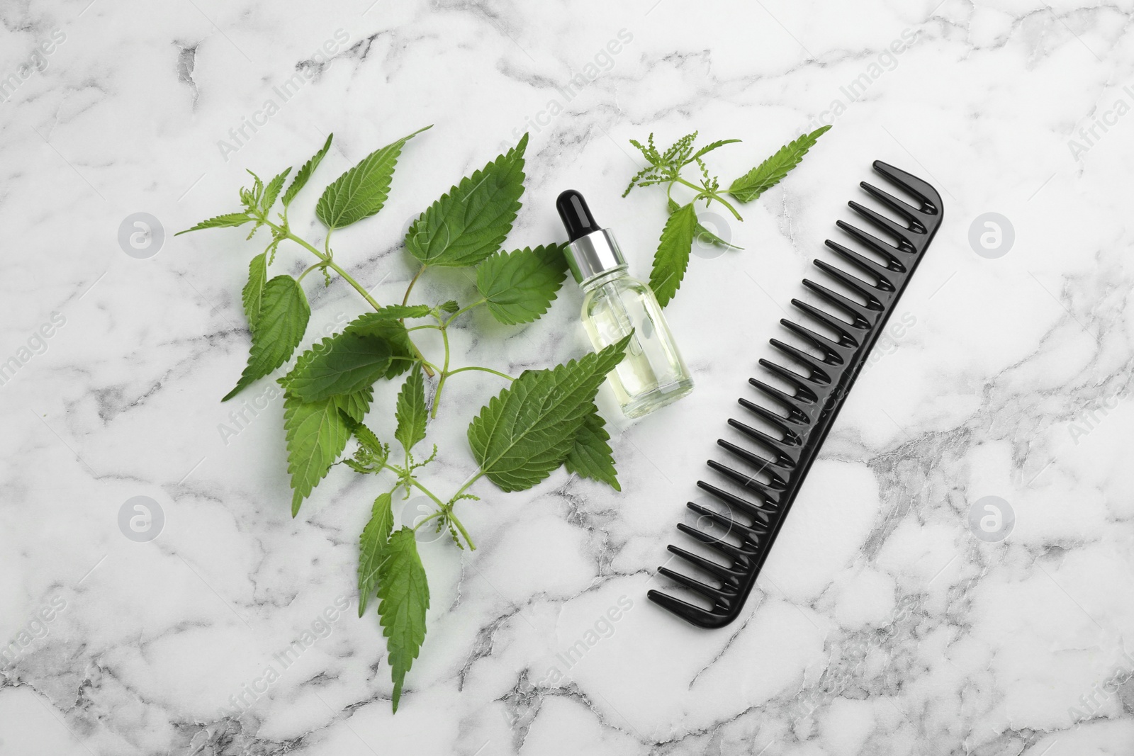 Photo of Stinging nettle, extract and comb on white marble background, flat lay. Natural hair care