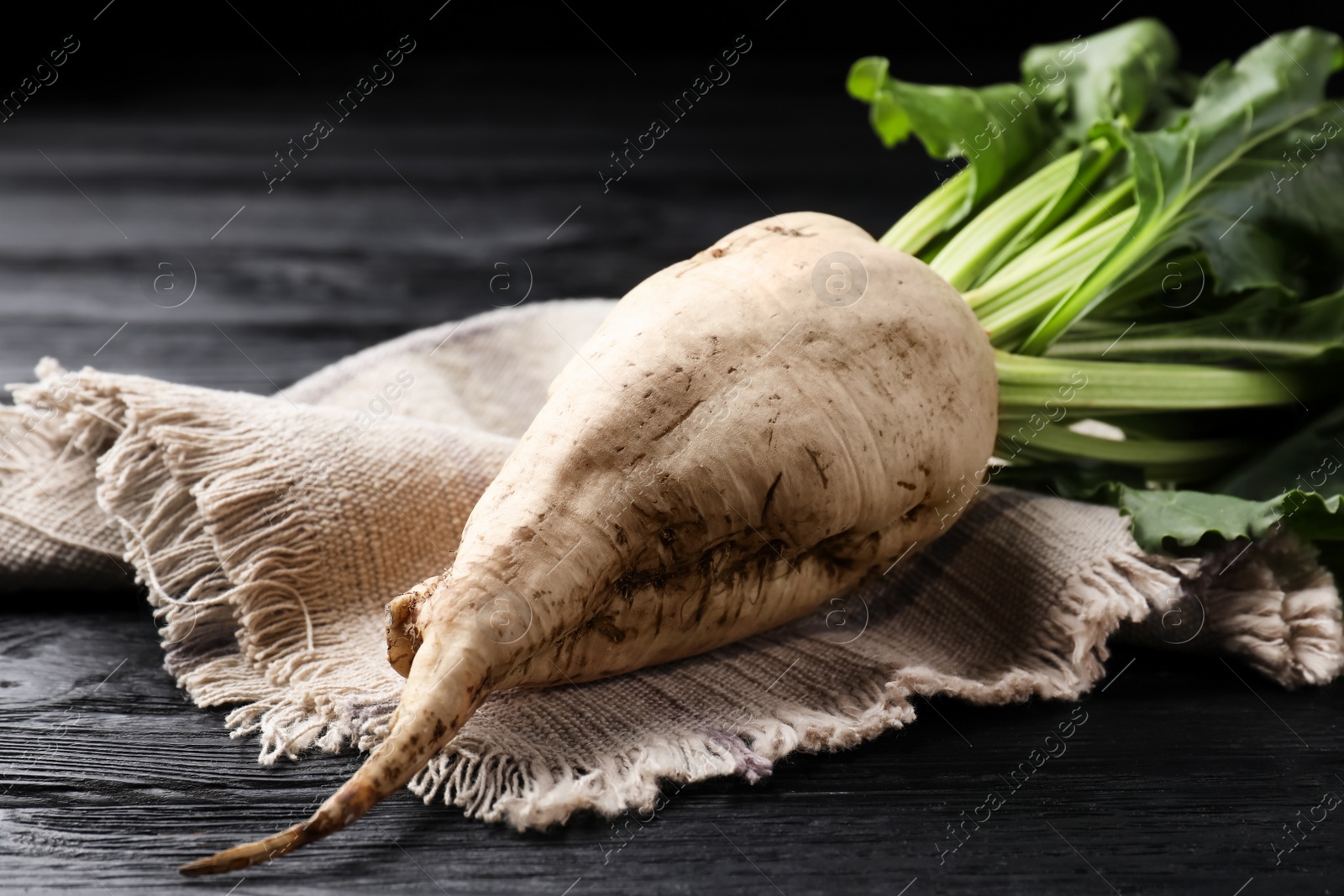 Photo of Fresh sugar beet with leaves on black wooden table, closeup