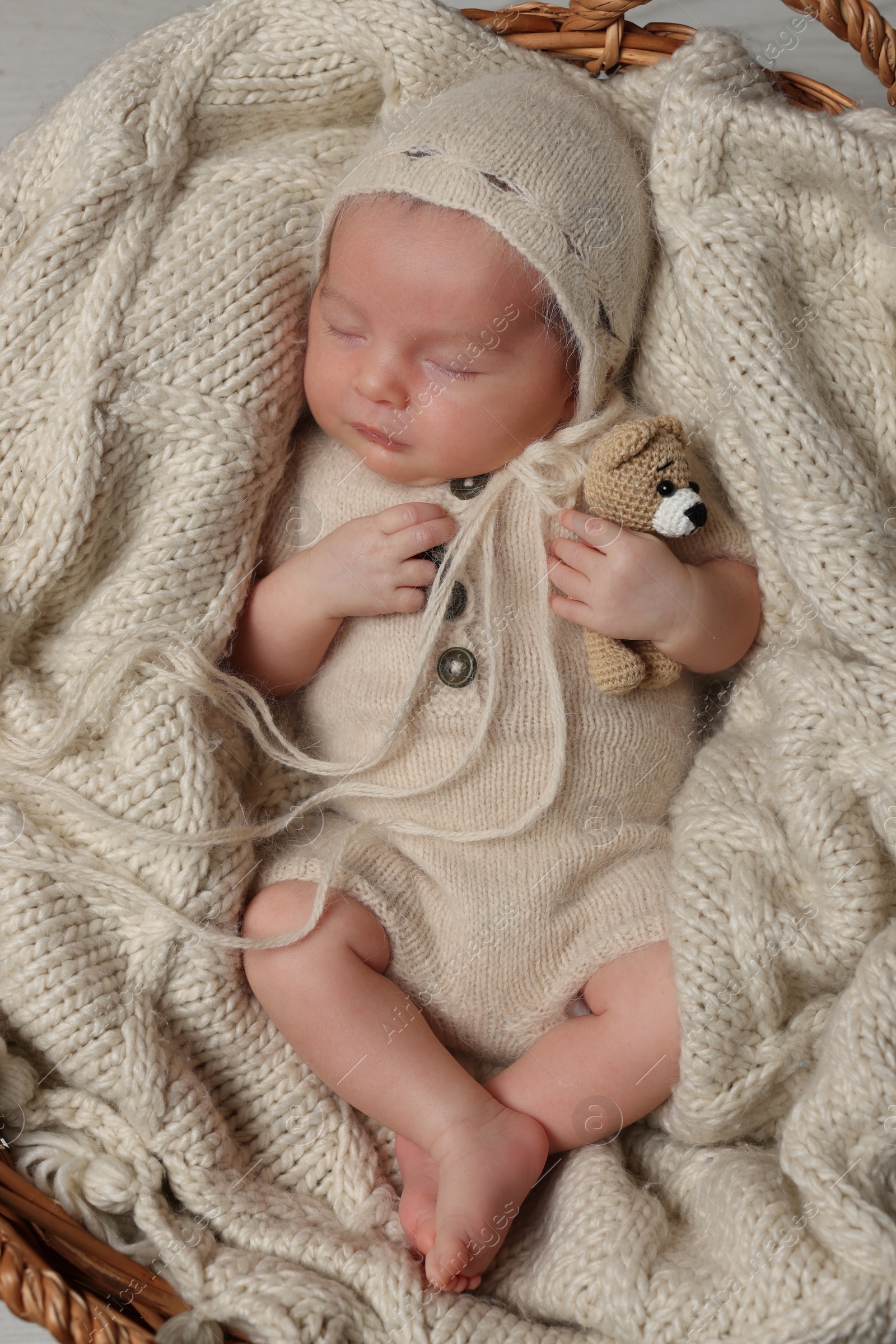 Photo of Adorable newborn baby with toy bear sleeping in wicker basket, top view