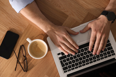 Man with laptop, cup of coffee and smartphone at wooden table, top view