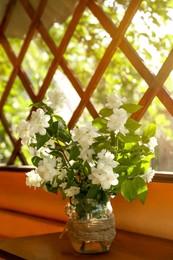 Photo of Bouquet of beautiful jasmine flowers in glass vase on wooden table indoors