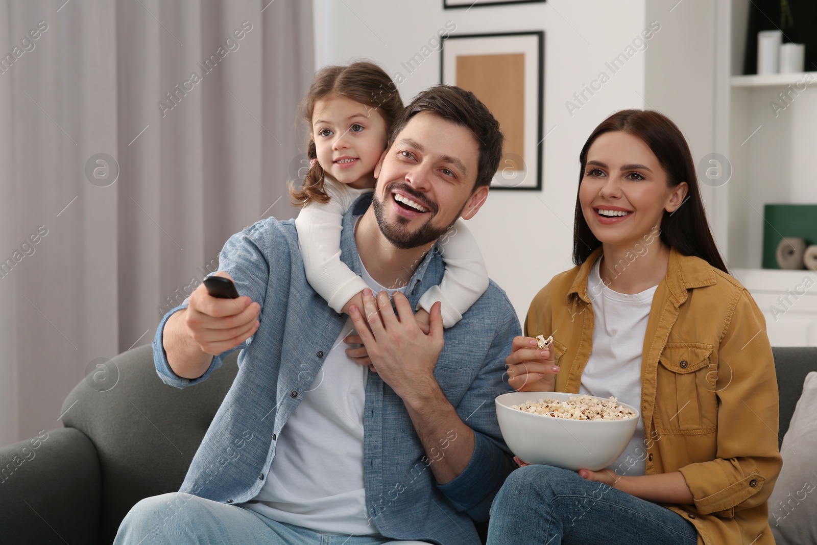 Photo of Happy family watching movie at home. Father changing TV channels with remote control