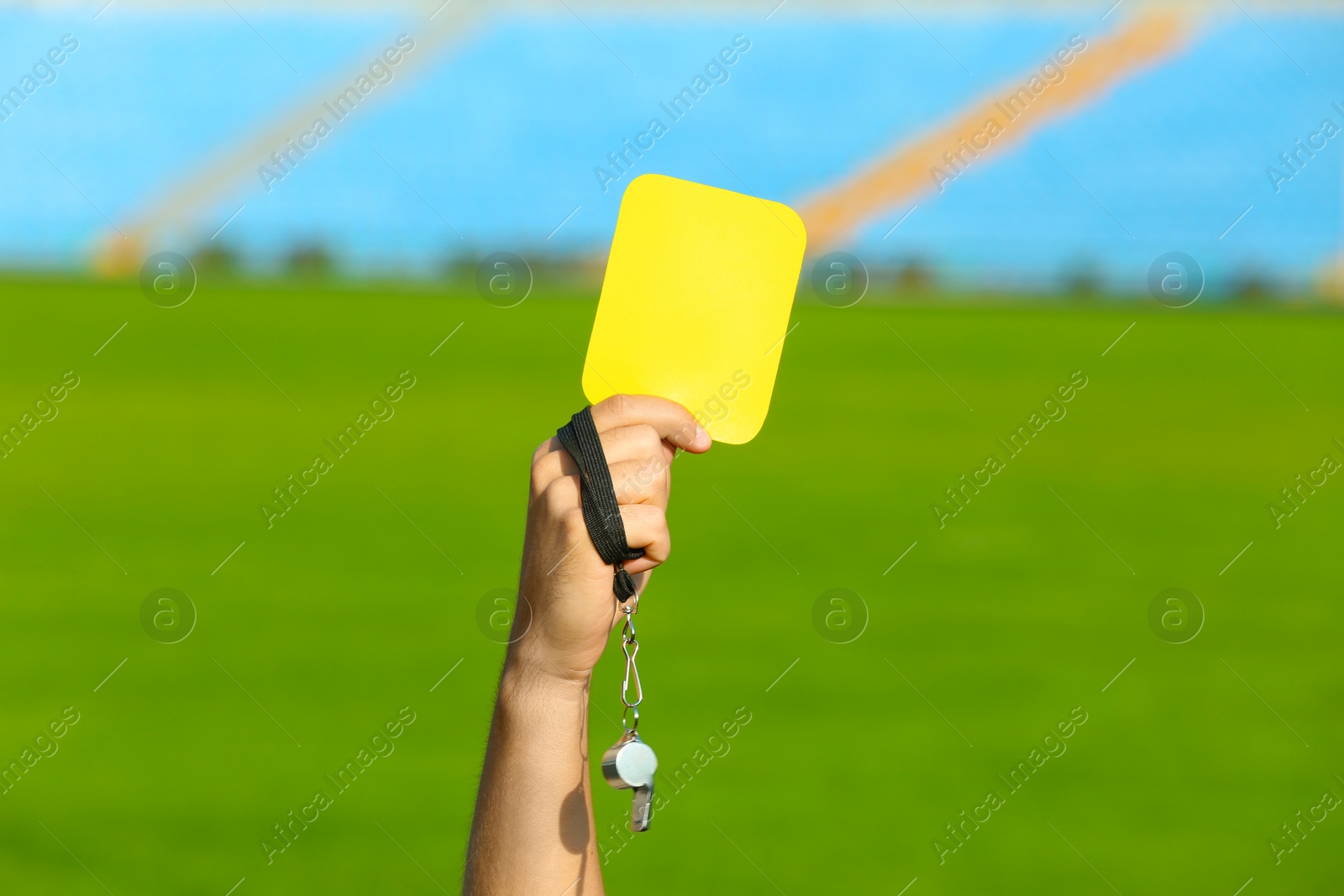 Photo of Football referee holding yellow card and whistle at stadium, closeup