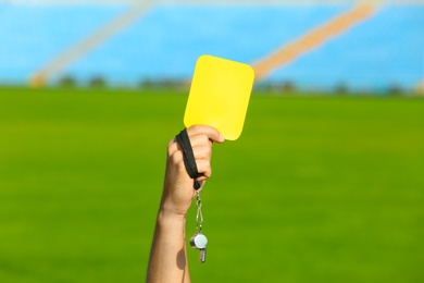 Football referee holding yellow card and whistle at stadium, closeup