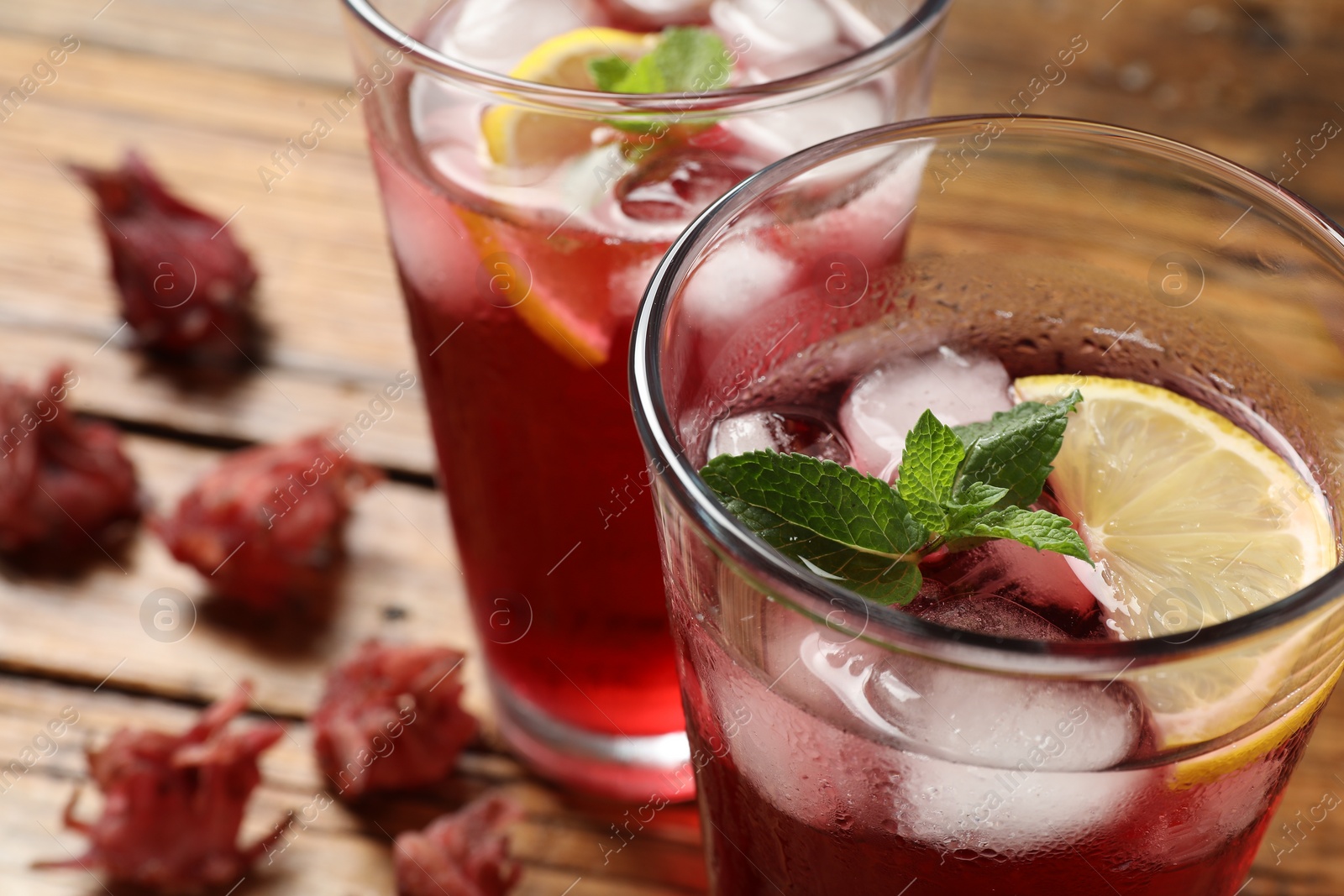 Photo of Glass of delicious iced hibiscus tea on wooden table, closeup. Space for text