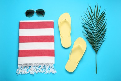Beach towel, flip flops and sunglasses on light blue background, flat lay