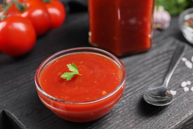 Photo of Delicious ketchup, parsley and spoon on black wooden board, closeup. Tomato sauce