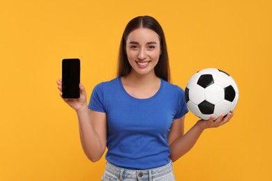 Happy fan holding soccer ball and showing smartphone on yellow background