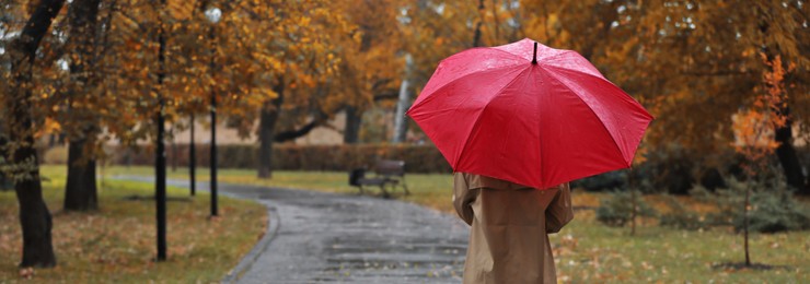 Image of Woman with umbrella in autumn park on rainy day, back view and space for text. Banner design