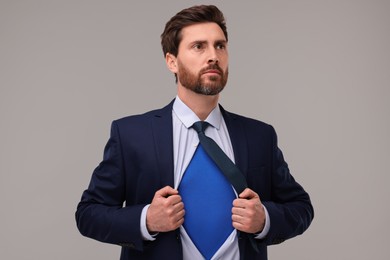 Confident businessman wearing superhero costume under suit on beige background