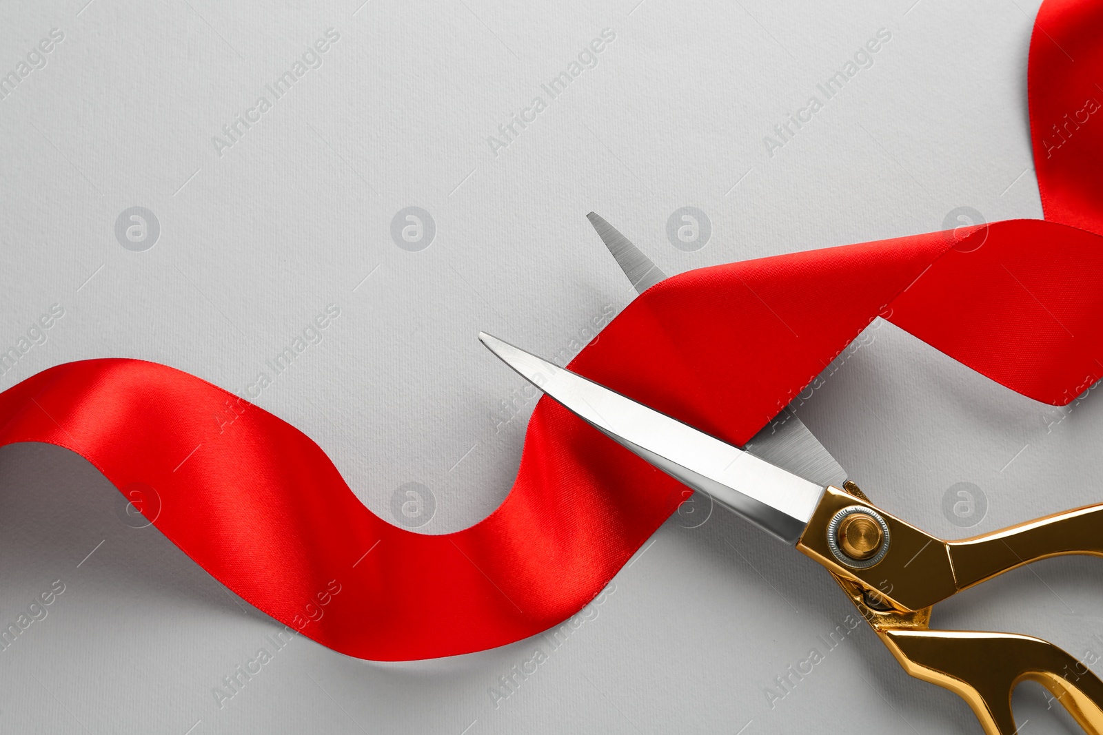 Photo of Red ribbon and scissors on light grey background, top view. Space for text