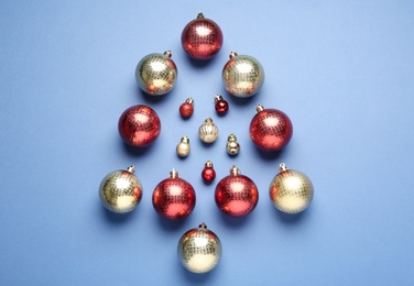 Photo of Christmas tree shape made of decorative balls on blue background, flat lay