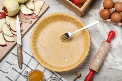 Flat lay composition with raw dough, fork and ingredients on white wooden table. Baking apple pie