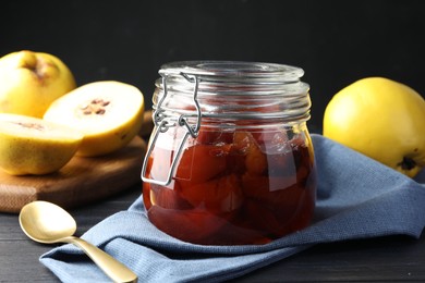 Quince jam in glass jar, spoon and fresh raw fruits on grey table, closeup