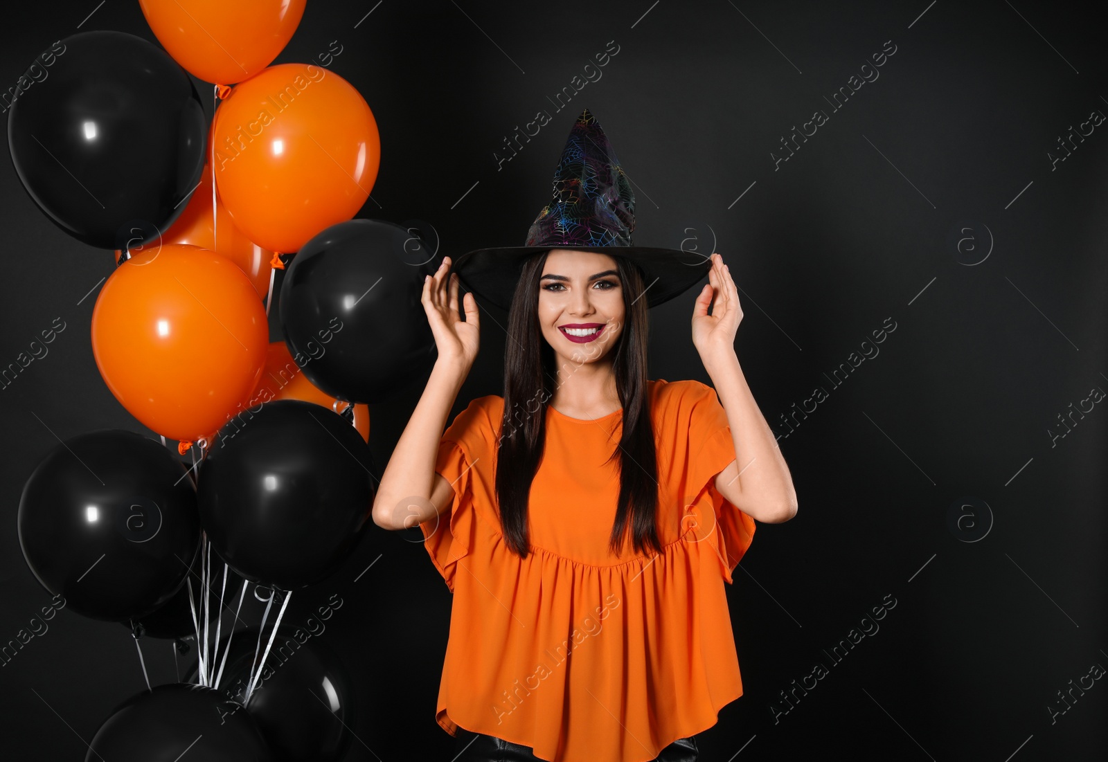 Photo of Beautiful woman wearing witch costume with balloons for Halloween party on black background