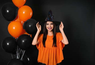 Photo of Beautiful woman wearing witch costume with balloons for Halloween party on black background