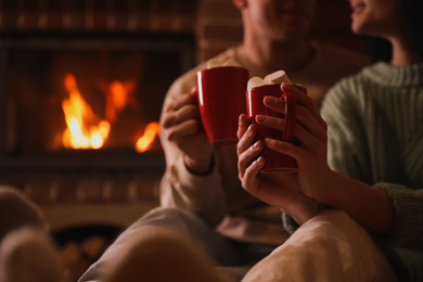 Photo of Lovely couple with sweet cocoa near fireplace indoors, closeup