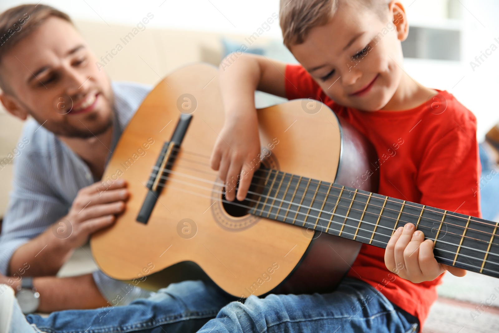 Photo of Father teaching his little son to play guitar at home