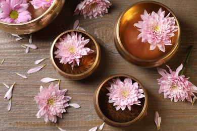 Tibetan singing bowls with water and beautiful flowers on wooden table, flat lay