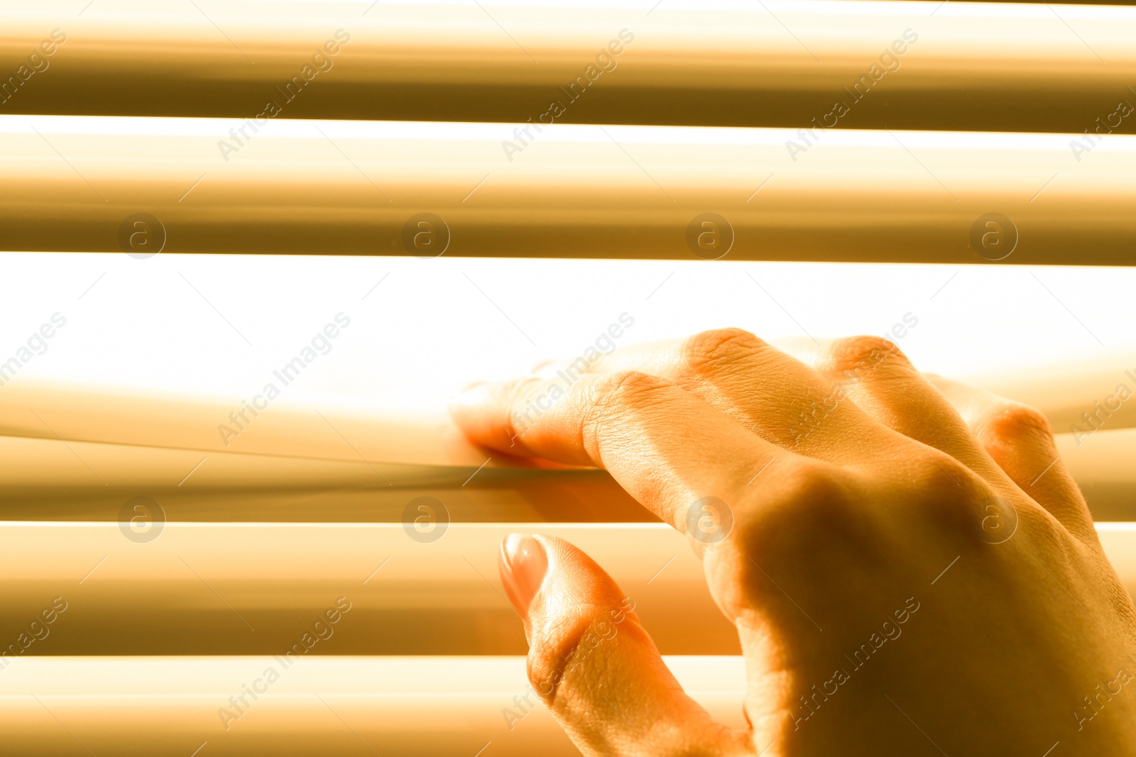 Photo of Woman separating slats of white blinds indoors, closeup