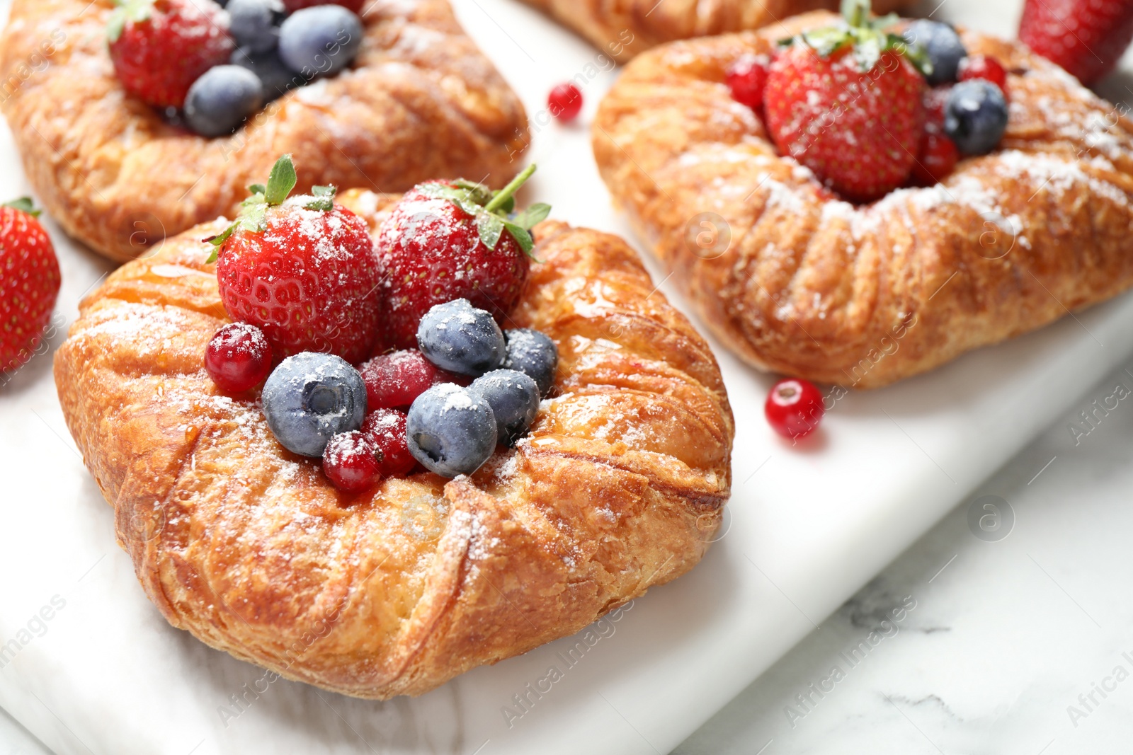 Photo of Fresh delicious puff pastry with sweet berries on white marble board, closeup