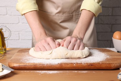 Woman kneading dough at wooden table near white brick wall, closeup