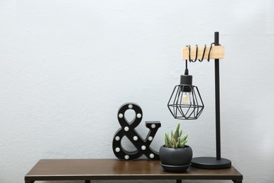 Photo of Beautiful plant in pot, lamp and decor on wooden table near light wall indoors, space for text. Interior accessories